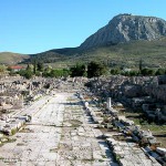 wide paved ancient street with sidewalks below a tall mountain