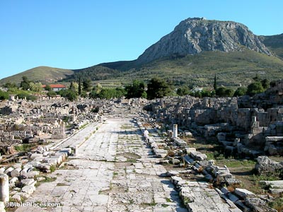 wide paved ancient street with sidewalks below a tall mountain