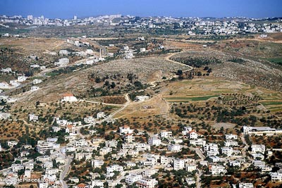 View from airplane of a hilly region covered in modern buildings and trees, with a relatively bare hill in the middle