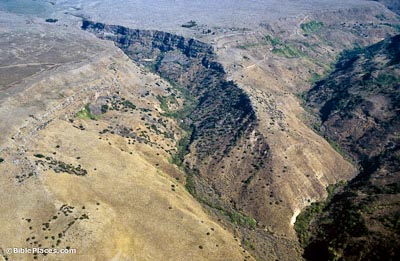 View from airplane of a ridge surrounded on three sides by valleys, the hills are mainly brown with some scattered plants