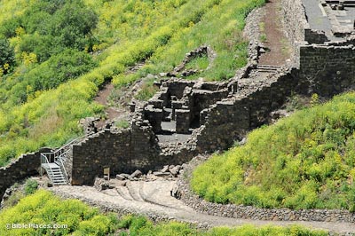 A grassy slope with a stone path leading up to a roofless, stone structure with walls dividing the space into different rooms