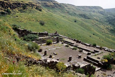 A rectangular stone foundation nestled on a grassy slope, parts of steps and columns jut from the structure