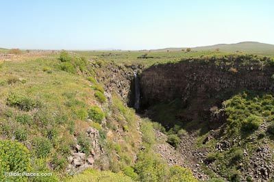 A view overlooking a valley that comes to a point at one end where a tall narrow waterfall streams down the cliff